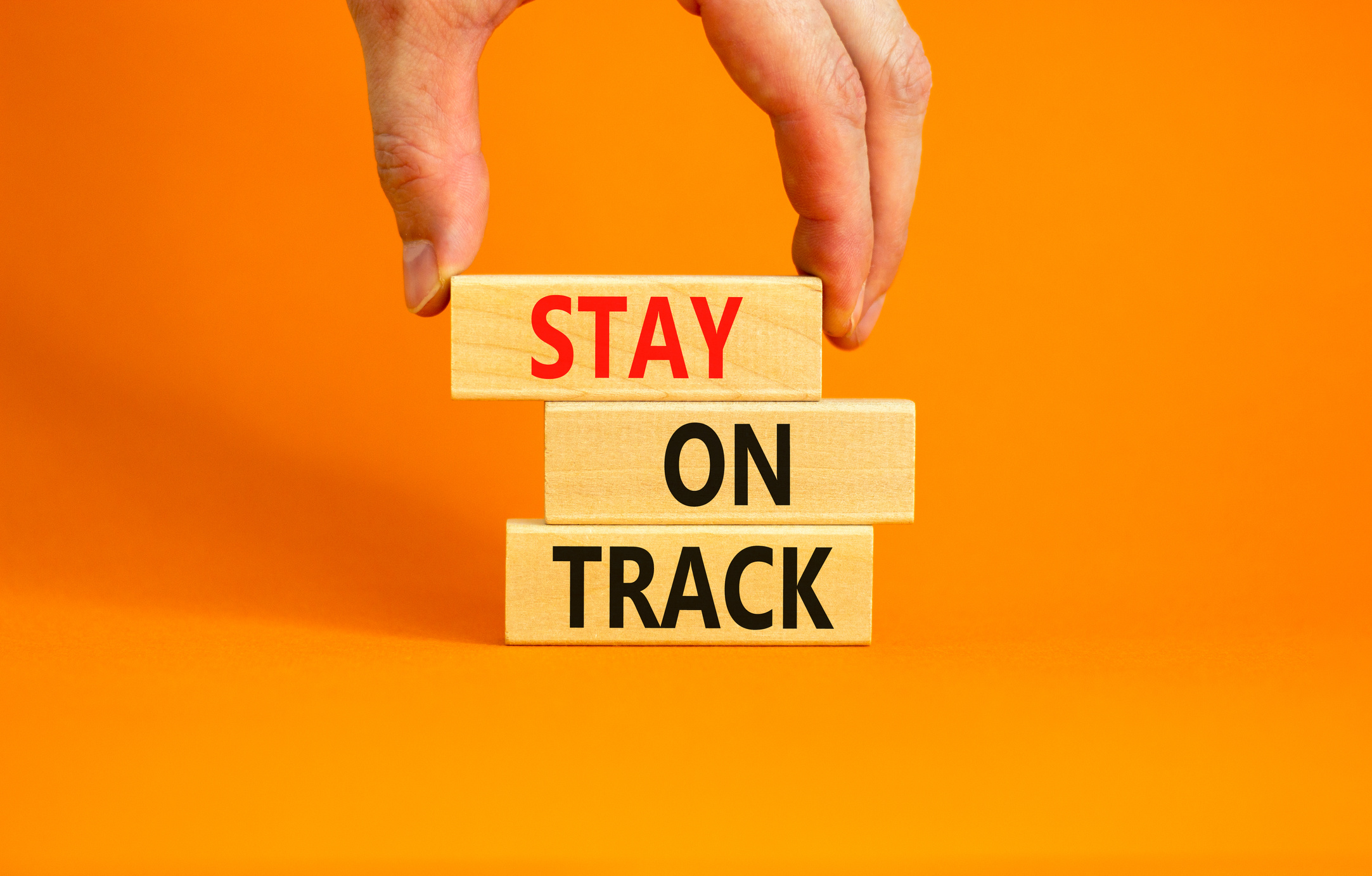 Stay on track symbol. Concept words Stay on track on wooden blocks on a beautiful orange table orange background. Businessman hand. Business, motivational and stay on track concept. Copy space.